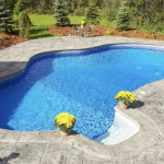 Curved inground swimming pool with stamped concrete patio and landscaping, showcasing backyard upgrade options for Rhode Island homes.